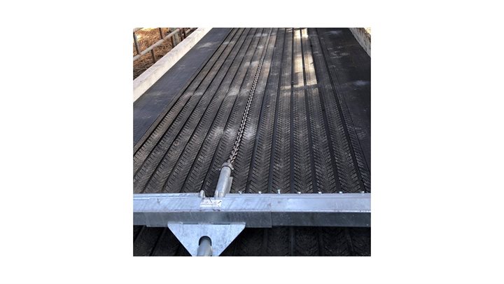 De afbeelding is een foto van een deel van de vloer in een stal met een mestschuif, zoals beschreven in de tekst.