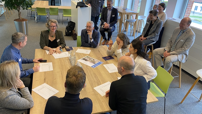 Op de afbeelding zit programma-DG Marjolein Jansen zit aan een tafel naast directeur Ruimte Marcel Schuring, wethouder Philip van Veller en andere medewerkers van gemeente Leidschendam-Voorburg en de bredere regio Haaglanden. Voor hen liggen enveloppen en invulformulieren van de fictieve casus die ze bespreken.