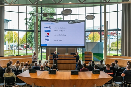 Foto van de statenzaal met de deelnemers en vooraan de sprekers.