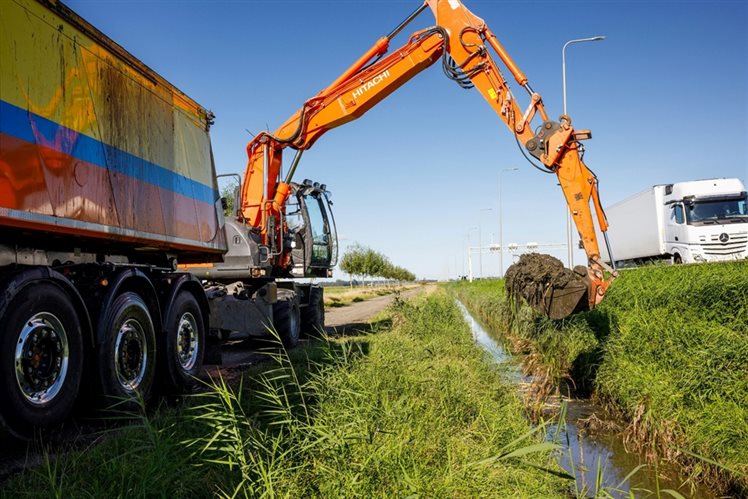 Een graafmachine schept bagger uit een sloot