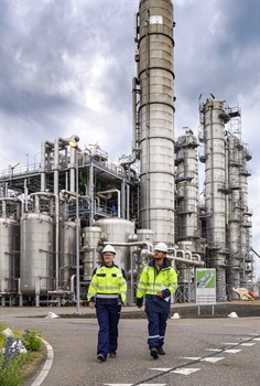 Reportagebeeld van een DCMR-inspectie bij Alco Energy Rotterdam; 2 mensen lopen weg van een installatie met tanks, leidingen en buizen.